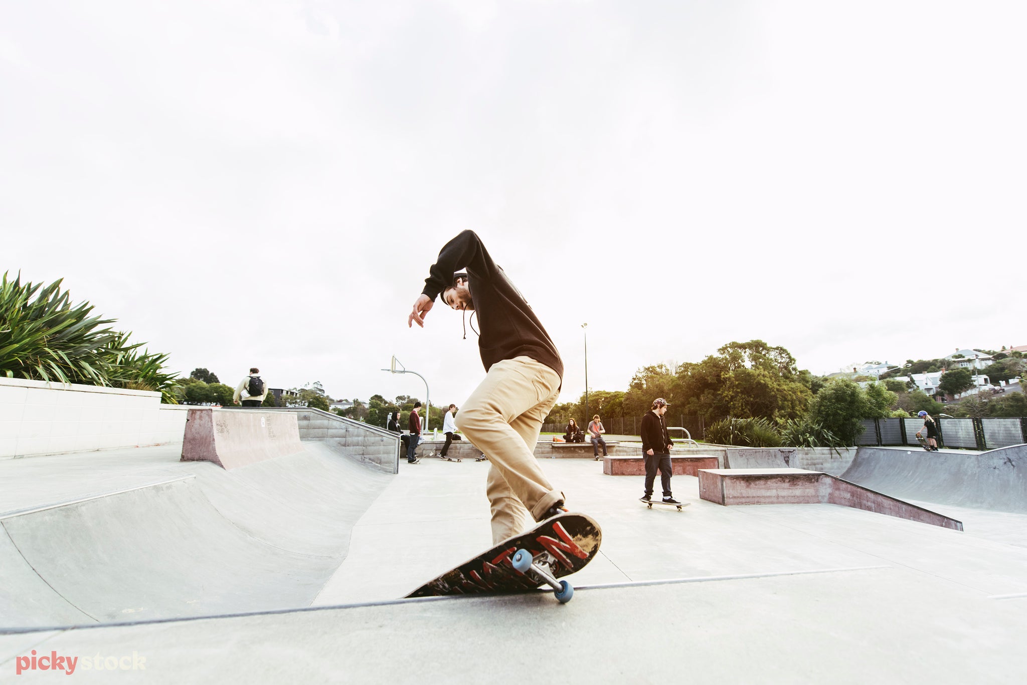 Skateboarder in chinos and a hoodie grinds a concrete ramp at a New Zealand skate park. 