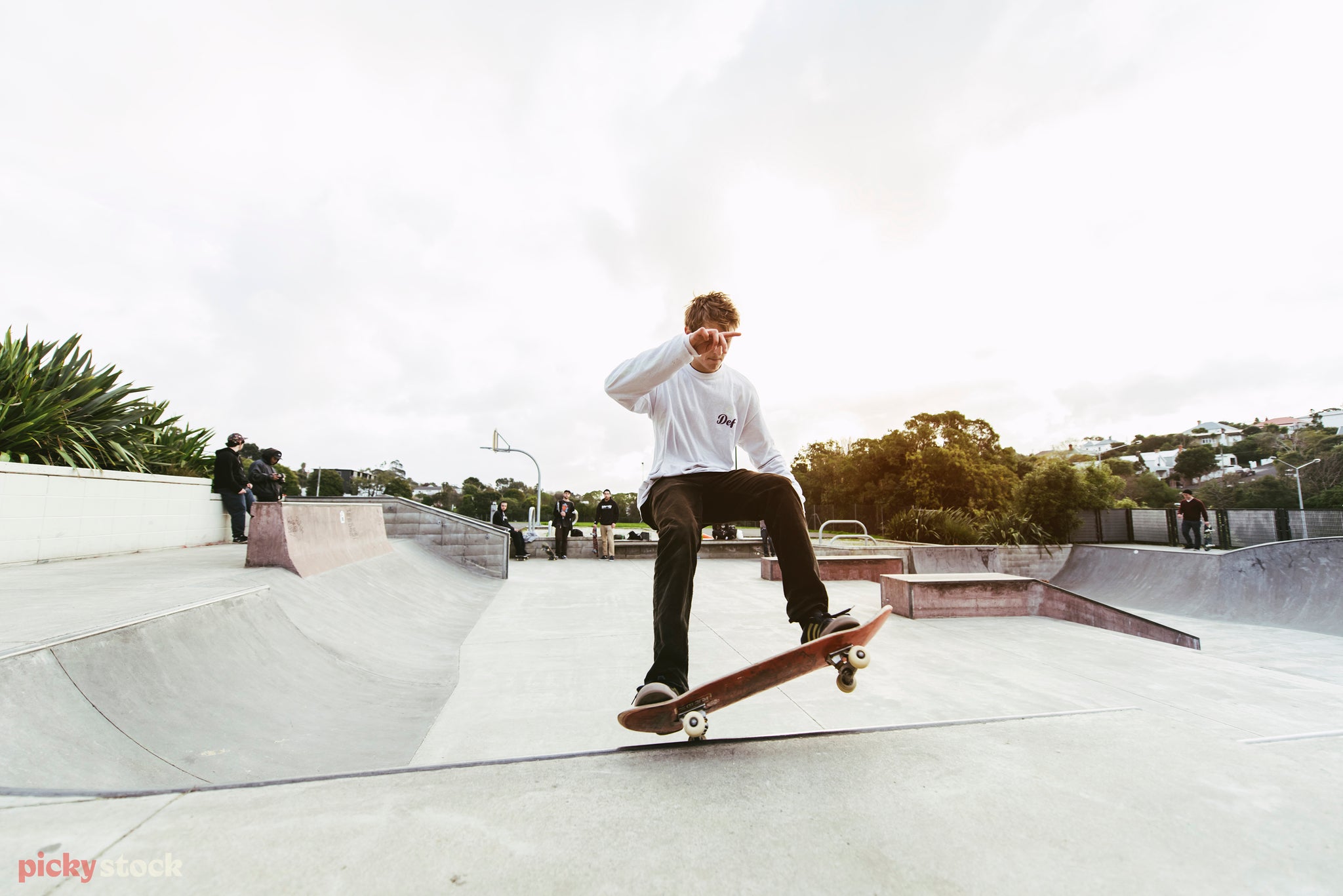 Skate boarder in dark pants and white shirt grinds a concrete rail in a New Zealand skate park.