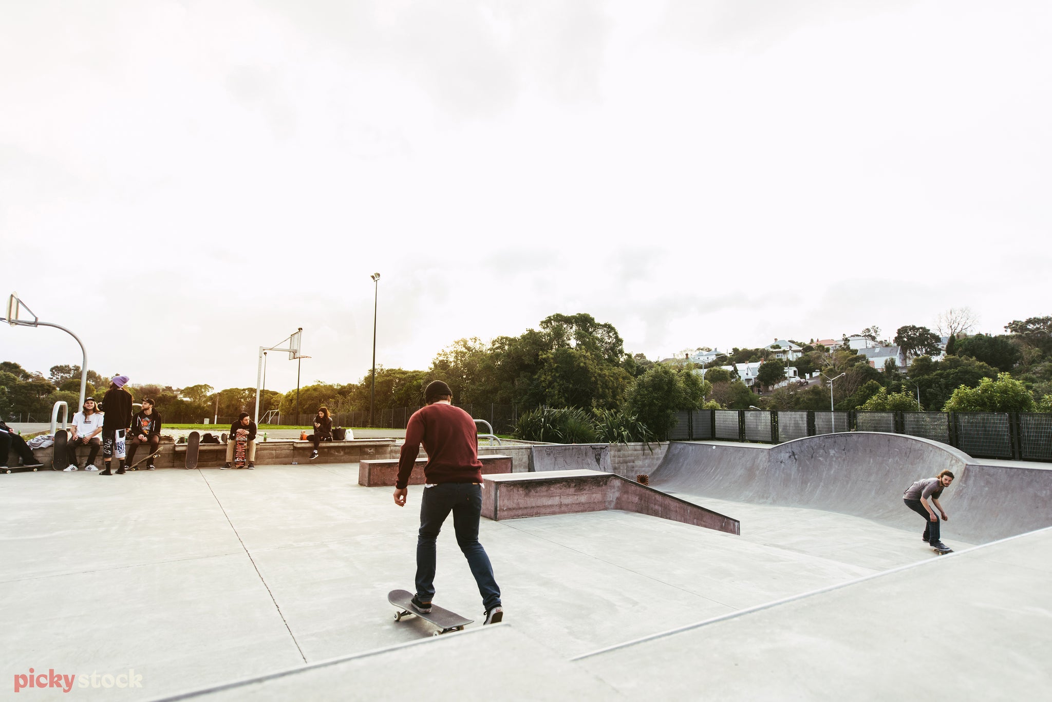 Skate boarder kicks across concrete skate park in Grey Lynn, in front of basketball court.