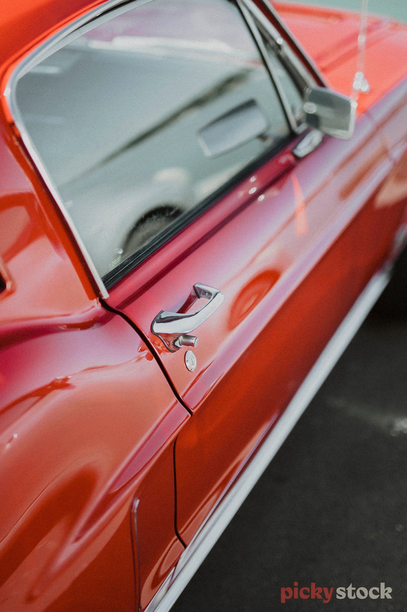 The right hand door of a red Mustang. Chrome door handle, wing mirror and accents.