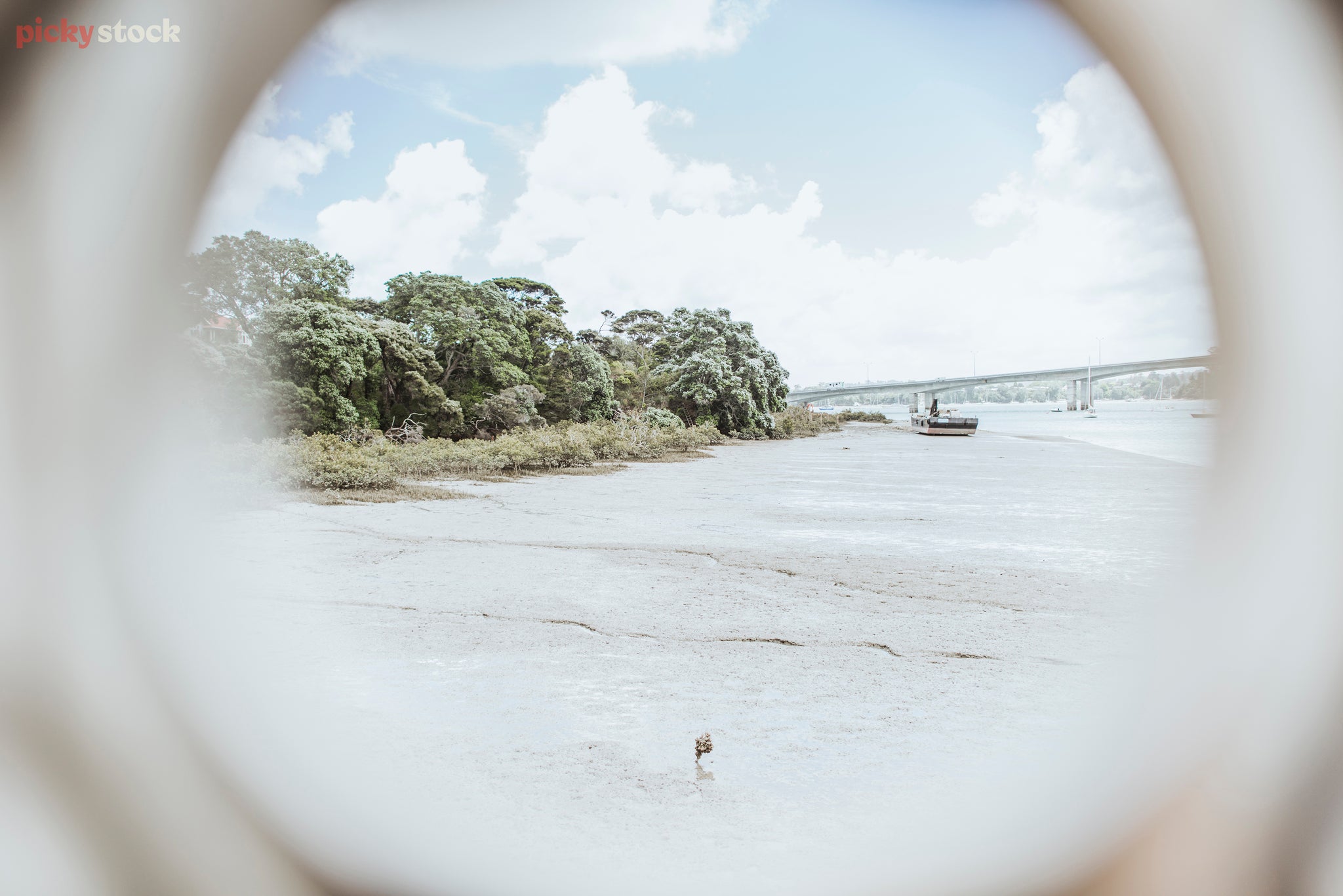 View through a porthole of a beach and a barge which is also beached. Mangroves grow closer to the shore.