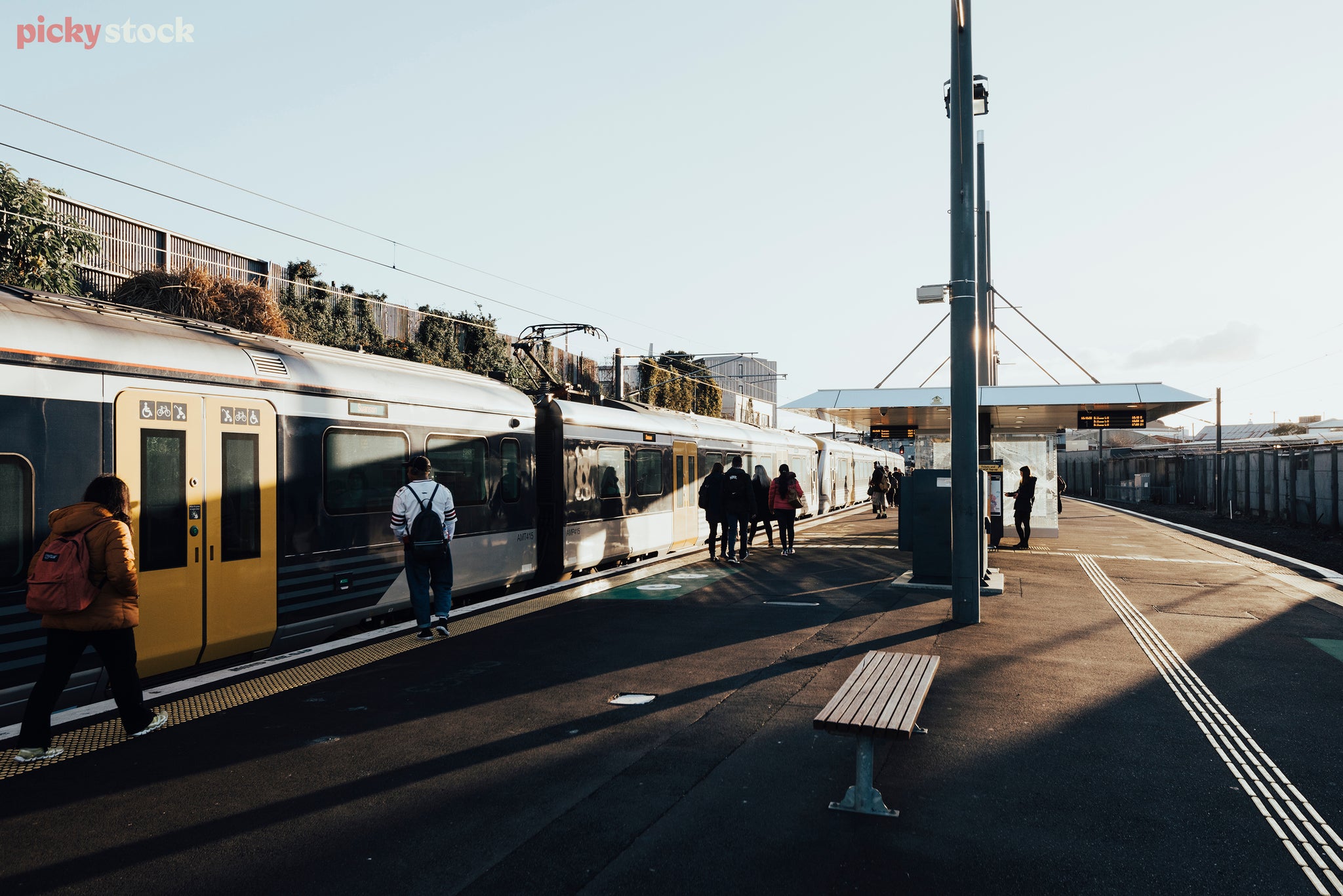 Late afternoon a blue and silver train stops at the original Mt Eden Station. People wait to board through the yellow doors.