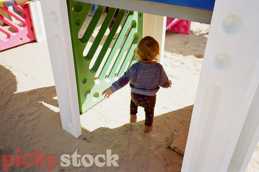 Toddler boy runs under a colourful playground on a sunny day.