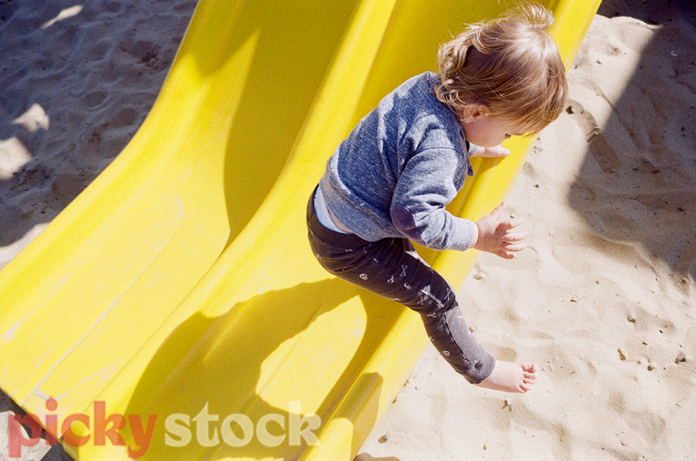 Toddler boy hops off a yellow slide.