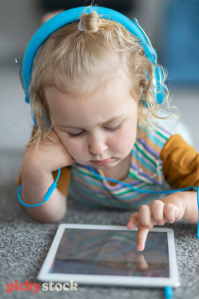 Girl lying on ground with blue headphones playing on iPad. 