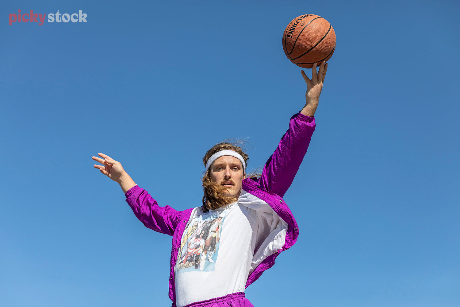 Man jumps in to frame wearing a bright purple eighties style jumpsuit, and sweatband.