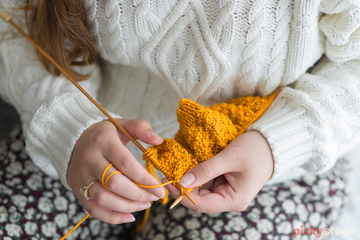 Unrecognisable young lady, knits a bright yellow jumper with knitting needles. 