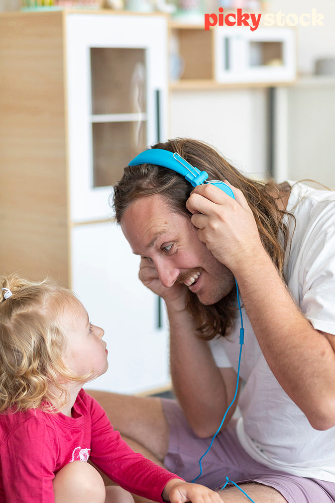 Small girl looking up at father who is wearing her blue headphones. Having a listen of her music. 