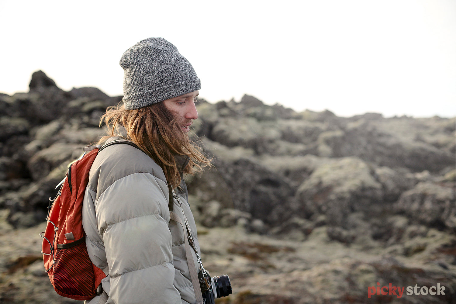 Young male with long hairr and beanie, wears a camera around neck while out exploring on a cold day. 