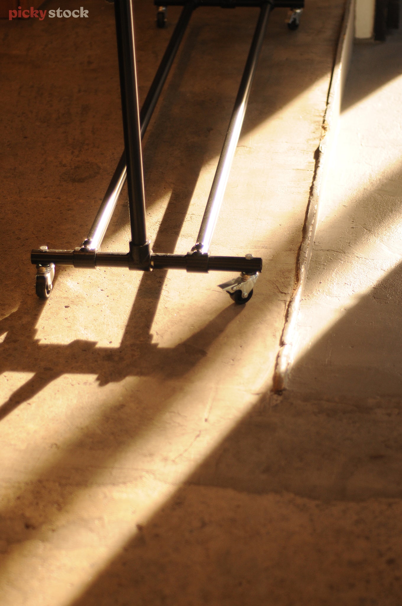 Portrait close-up of a metal clothing rack on the concrete floor, the sun casts two rays of light across the floor reflecting off the base of the clothing rack.
