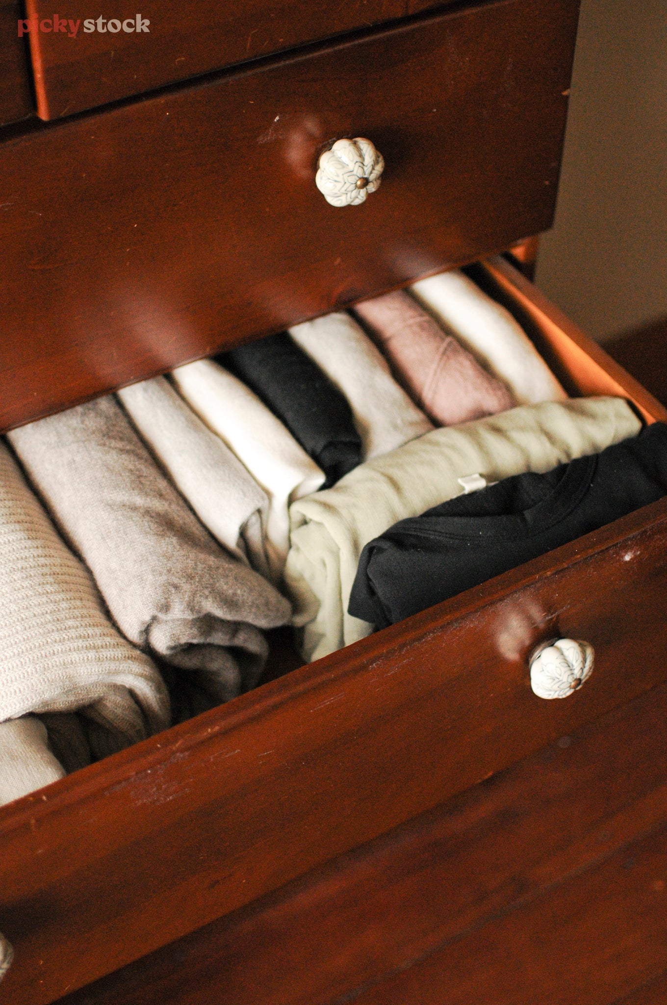 Portrait close-up of cold weather clothes neatly folded inside a wooden clothes dresser with white ceramic handles.
