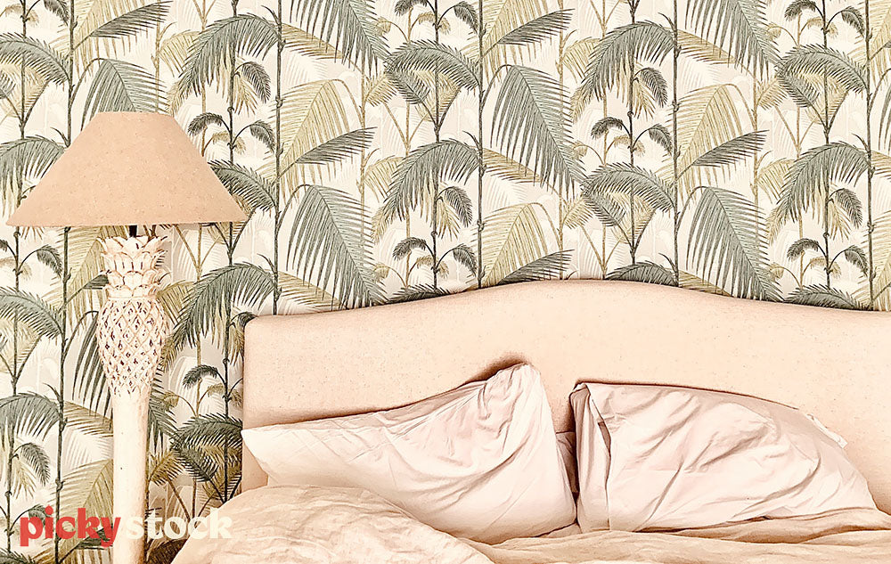 Unmade bed with pineapple lamp and green floral wallpaper.