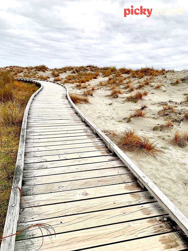 Wooden pathway with sand on it down through the sand dunes towards the water. 