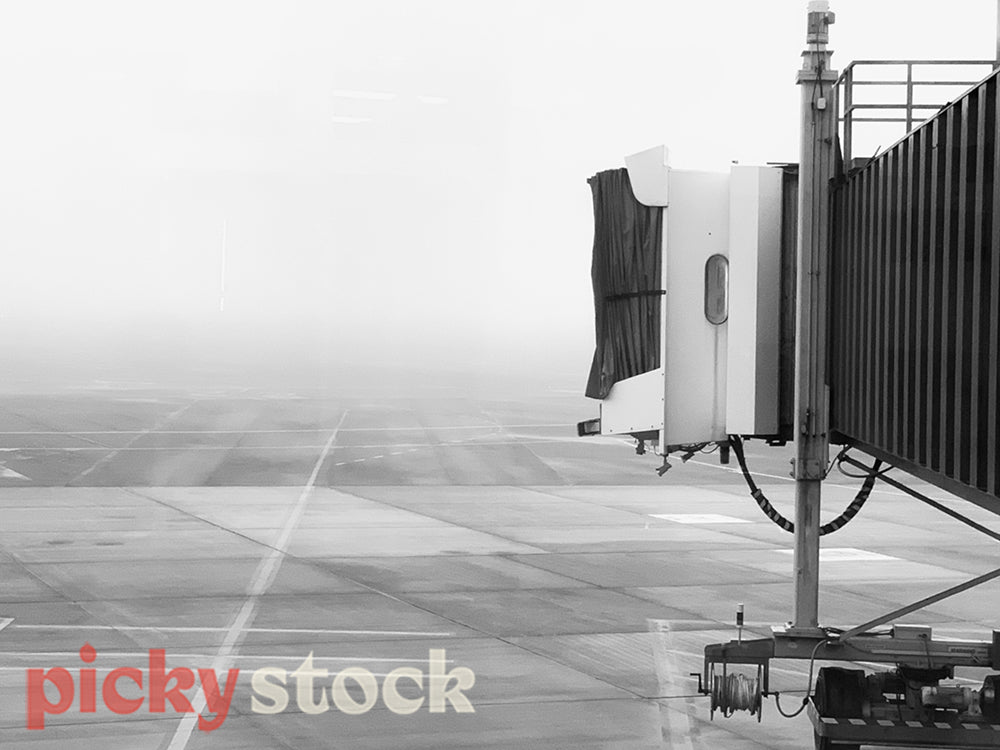 Black and white image of a aerobridge leading to no plane, on a foggy day. 