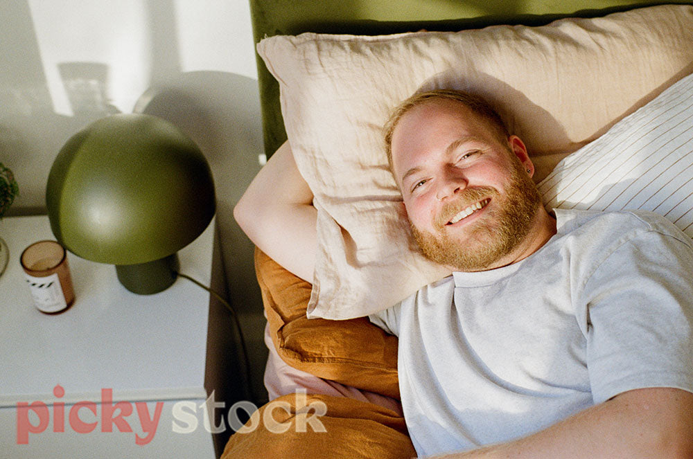 Gay man laying on a bed, laughing up at camera 