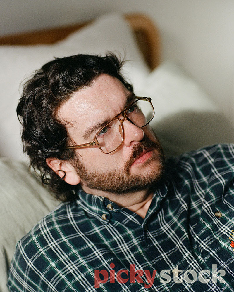 Gay man portrait, taken in a bedroom wearing glasses