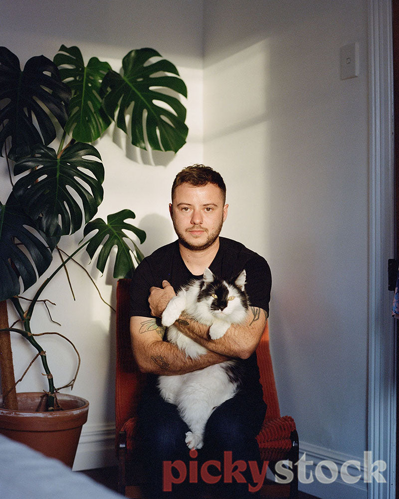 Trangender man portrait, holding a cat, taken in a bedroom