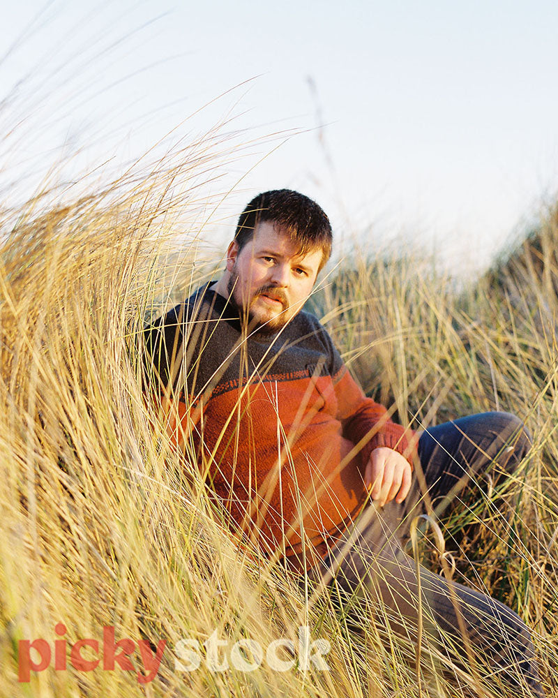Gay Man laying on a tussock beach under golden light.