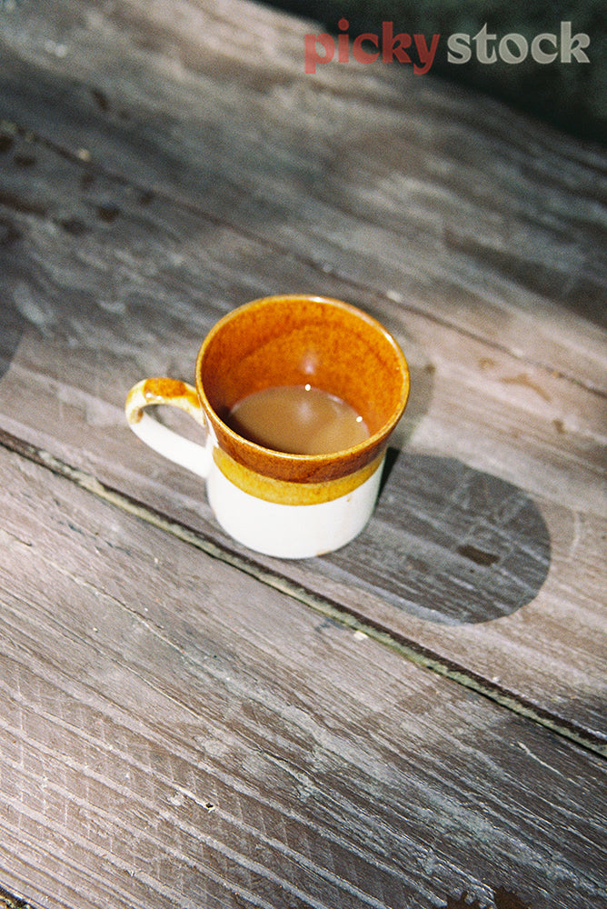 A cuppa in a retro mug, sitting on the wooden deck.  