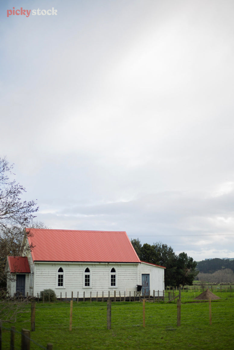 Old white farm church with red tin roof sits amongst the paddock.