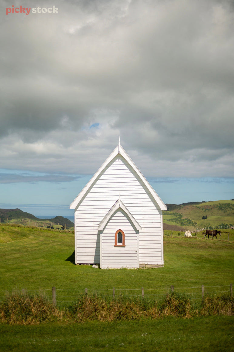 Little white chapel with pitch roof, stands out against the green rolling hills. 
