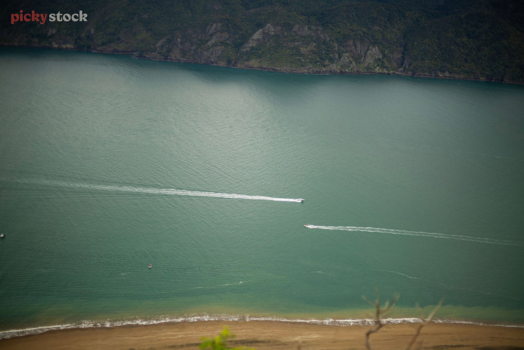Looking down at the water of Manukau Heads as the wakes of two boats cross paths. 