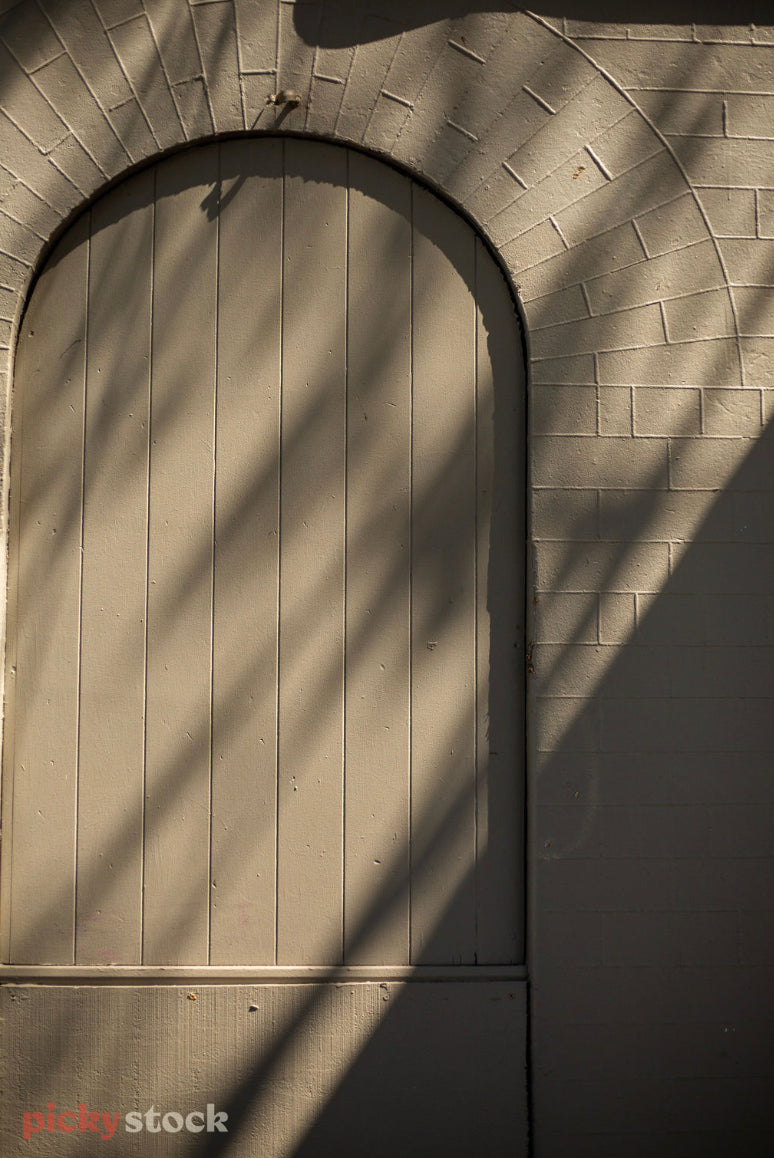 A light green wooden and brick archway is doused in shadow and light. 