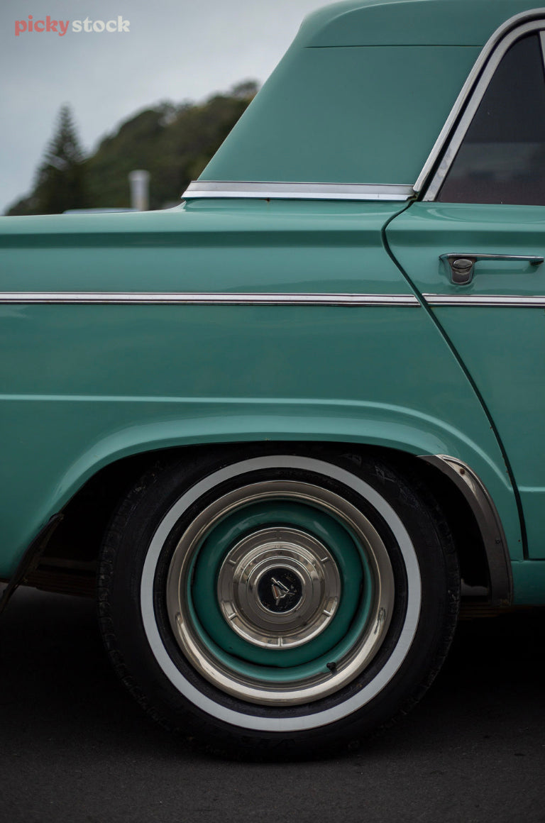 Close up image of wheel and back door of a mint green classic car.