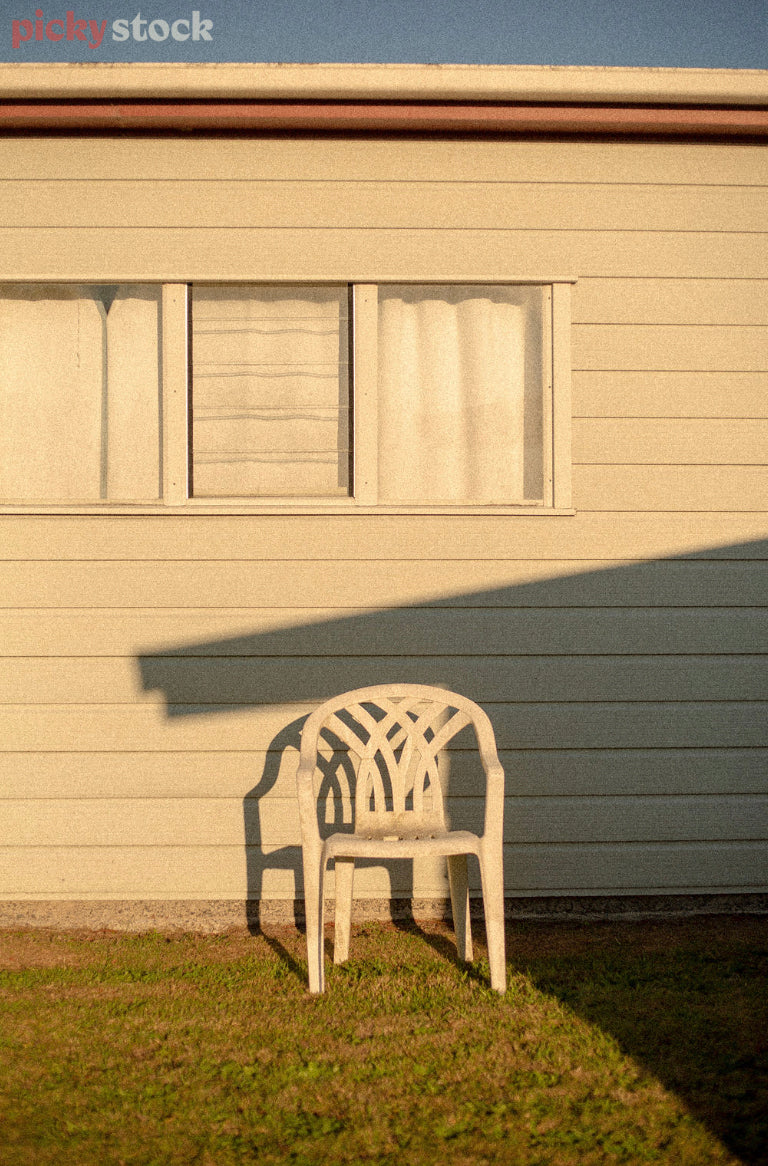 Plastic white chair sits on the lawn against a white garage in the afternoon light. 