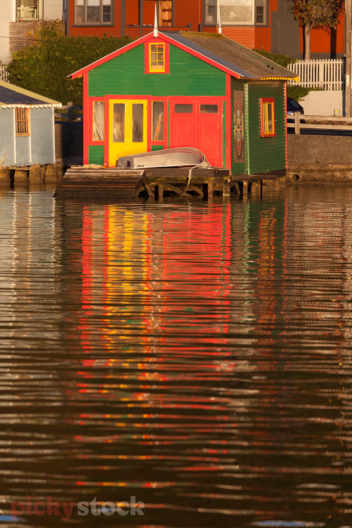 Colourful boadsheets along Wellington waterfront. Light reflections in the water, soft early evening light. Boadshed is red with green and yellow trim. 