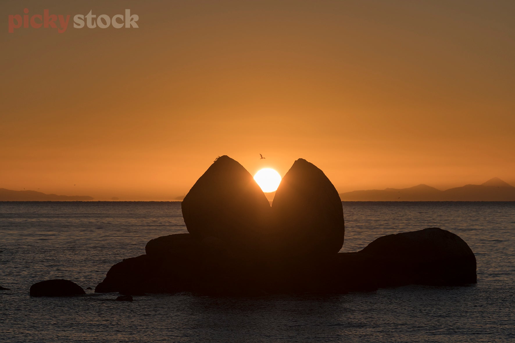 Sunrise at Split Apple Rock. Light perfectly connecting with split of the rock with light leaking through. Rock sitting in the middle of the ocean. Water is calm, early morning light. 