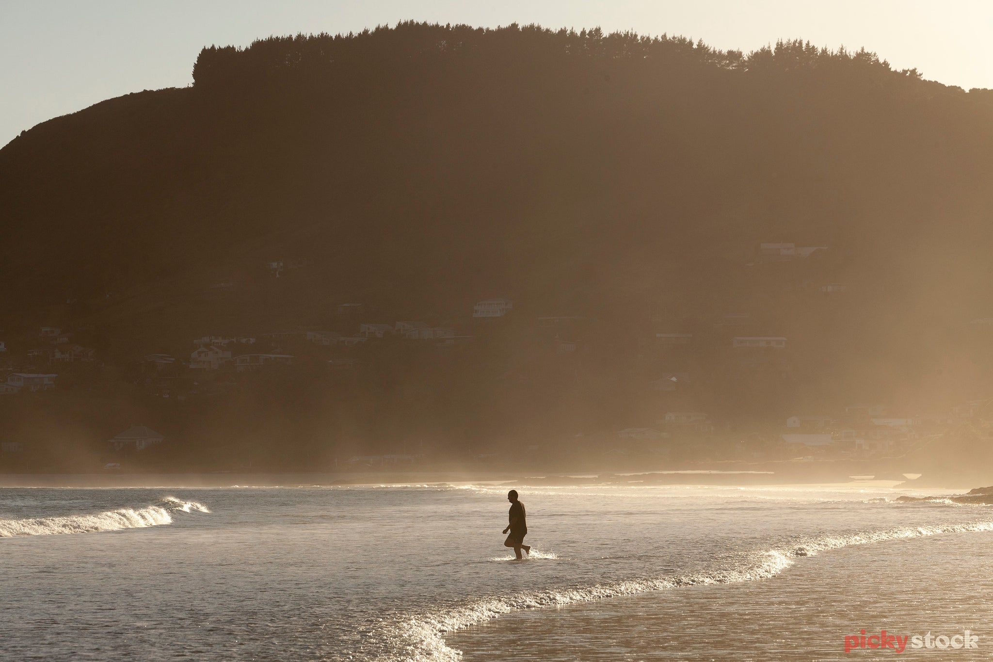 Early morning swimmer at Ahipara. Man walking into water. Large hill cliff in background. 