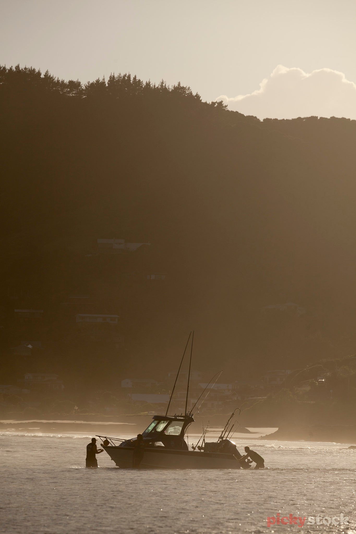 Boat being launched by two fishermen at sea in Ahipara in golden light. 