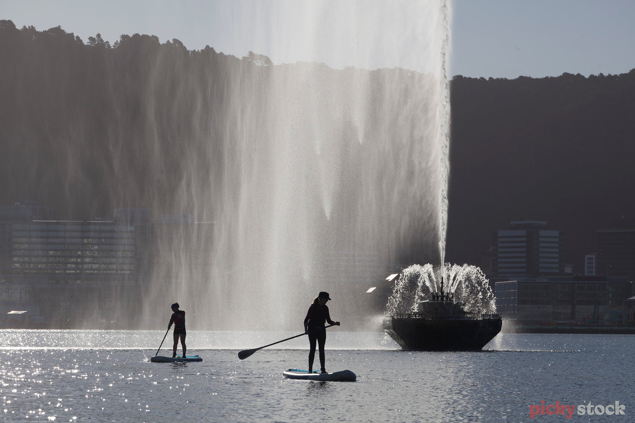 Two paddle Boarders paddle past the large waterfall pontoon at Oriental Bay Wellington. 