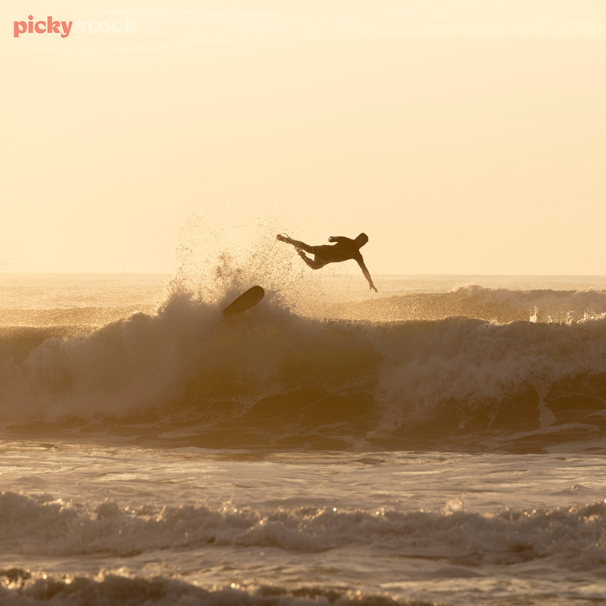 Sufer falling off surf board mid air, about to drop in to the surf. At golden hour - sunset / sunrise. 
