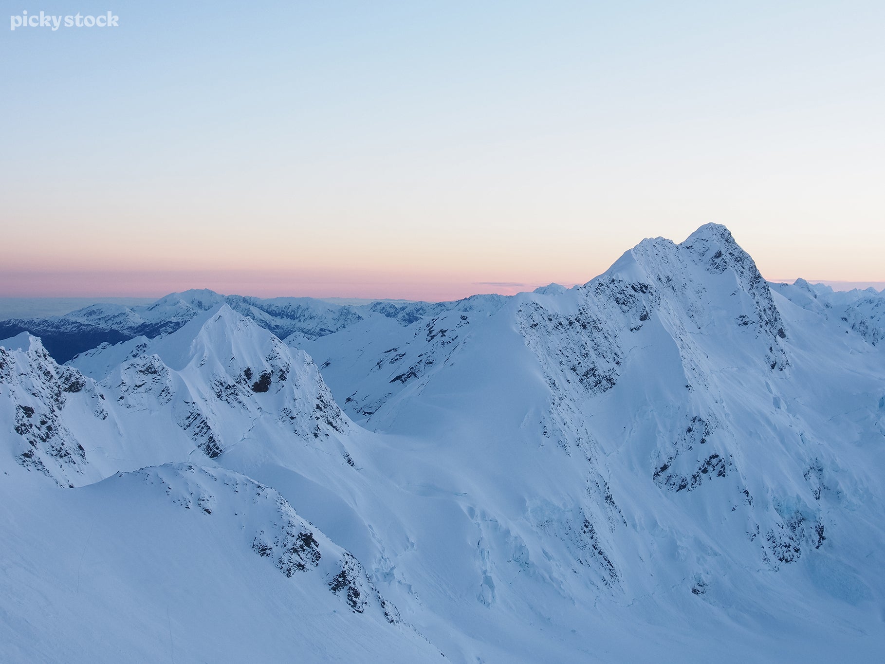 Landscape of a white snowy mountain range in a cool blue light with a soft red sky hanging far in the backgorund.