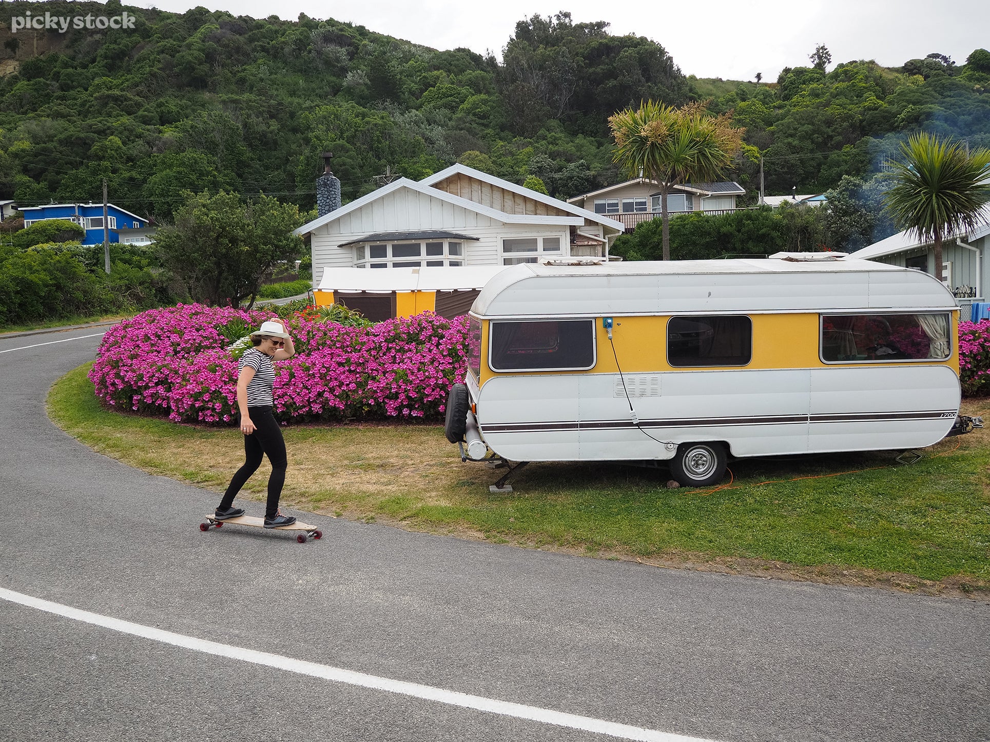 Guy longboarding on rural street. Passing caravan with yellow markers. 