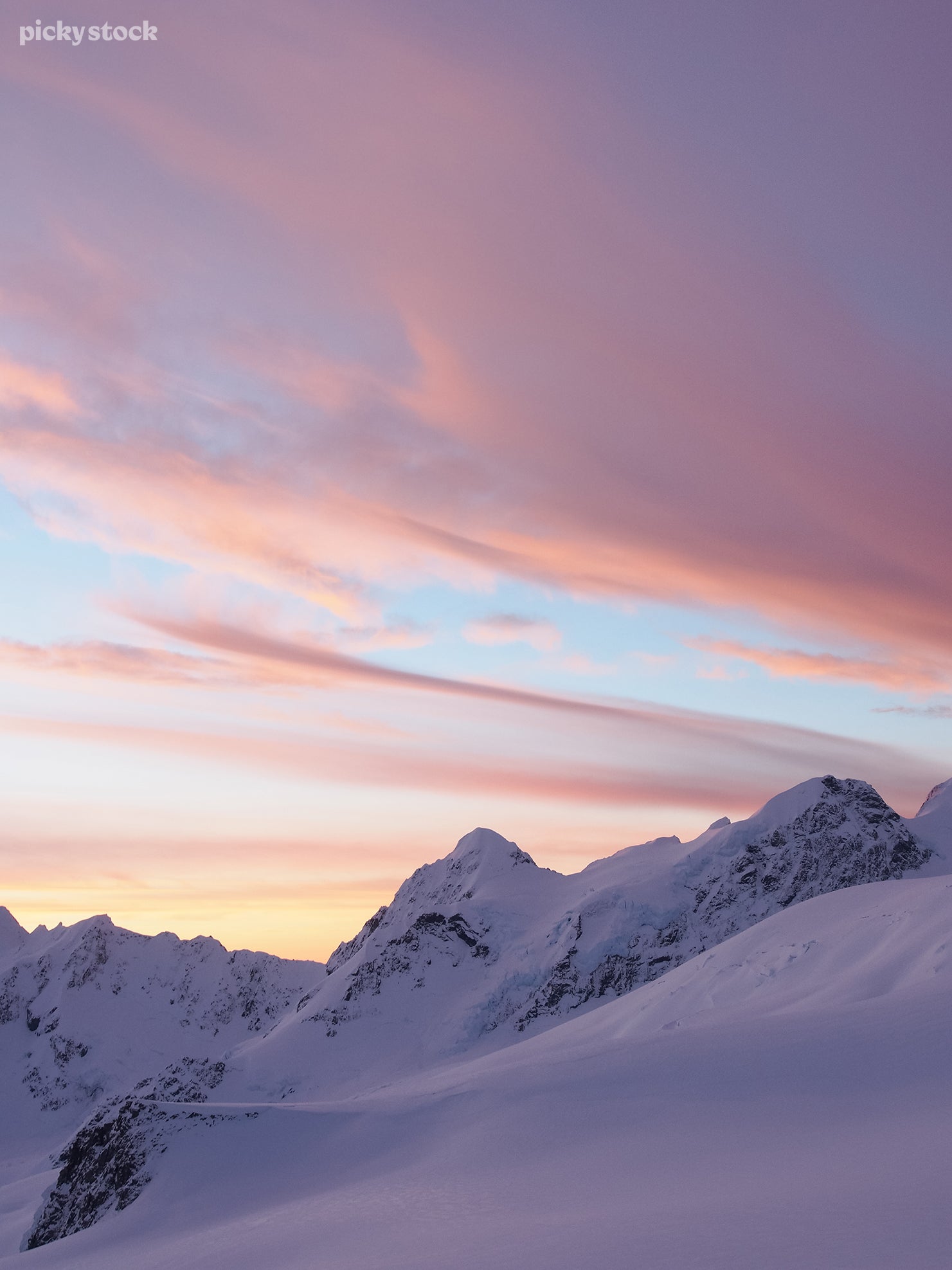 Portrait of snowy mountain top reflecting the vibrant hues of the afternoon sky. The snow casts shadows of bright hues of pink and blue that cascade across the sky.