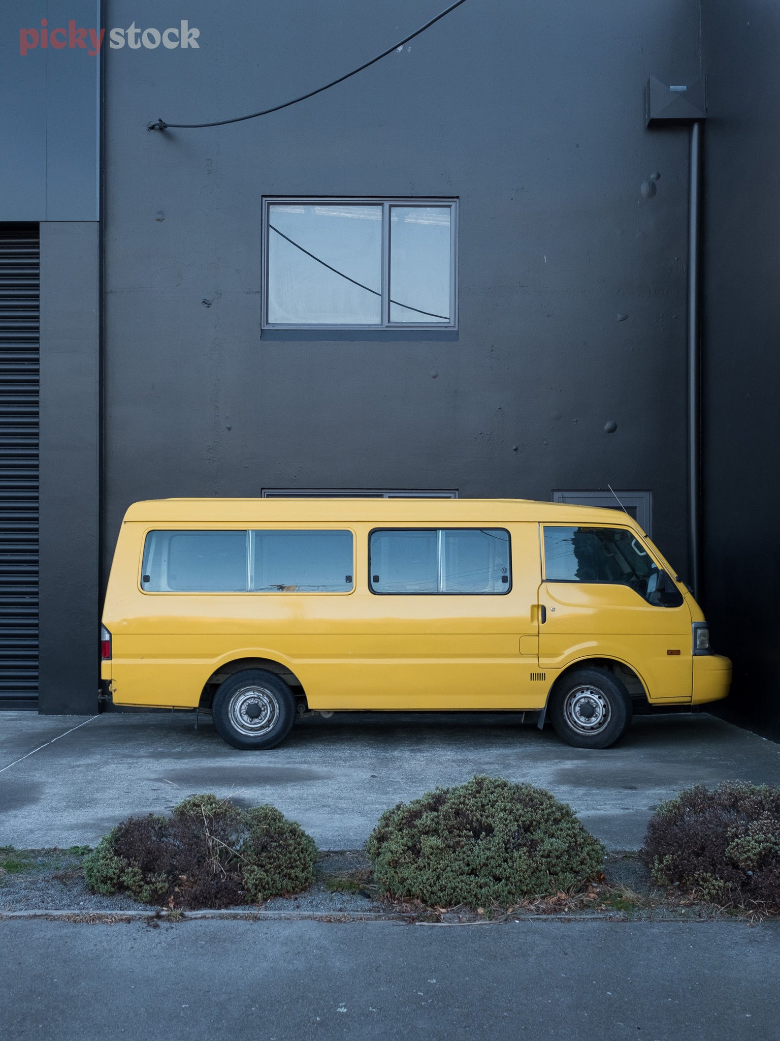 Graphic shot of bright yellow van set against a black-painted concrete building in an urban setting. 