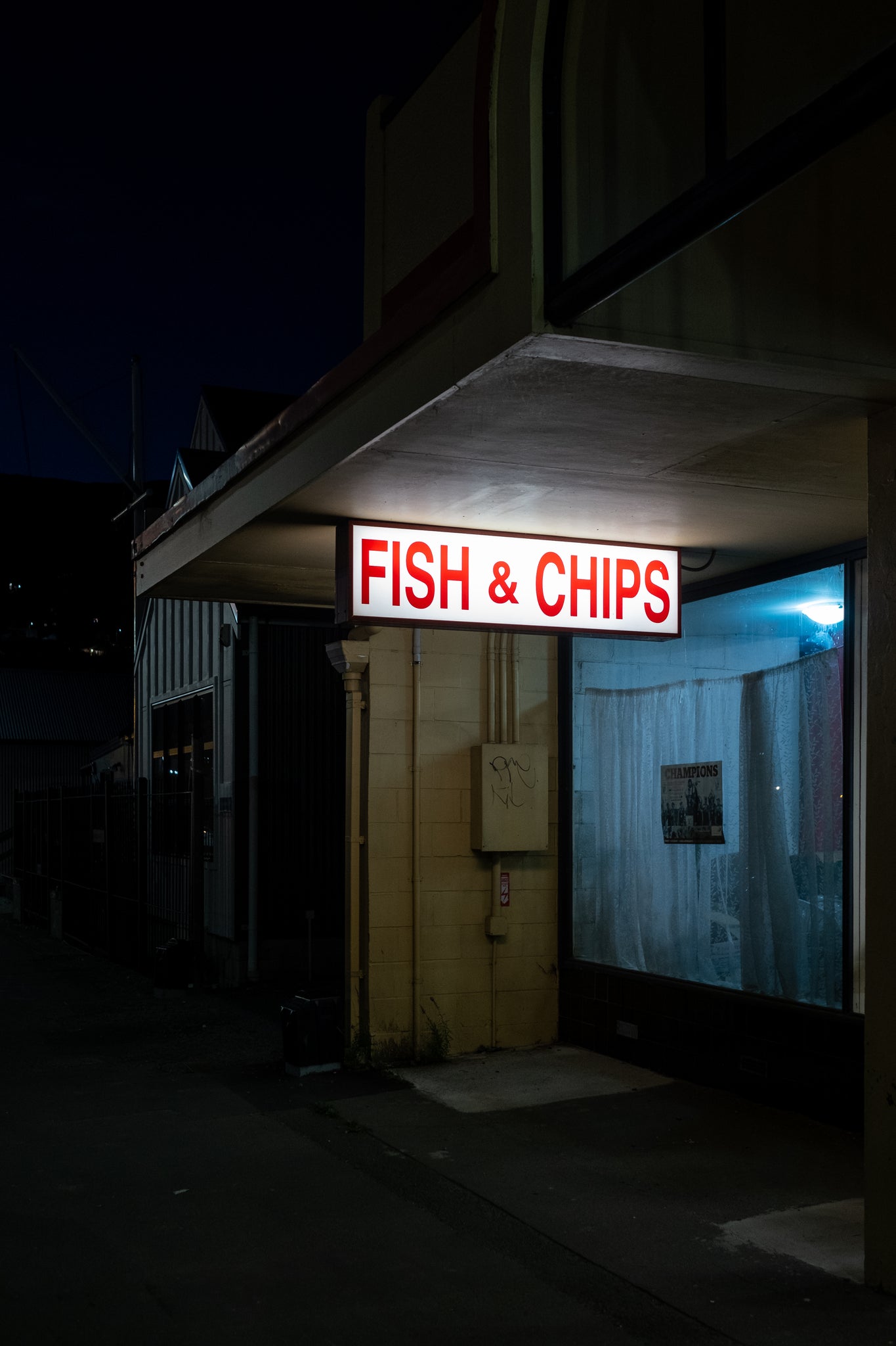 Fish and Chip shop, at closing. Dark black night sky. Fish and Chips illuminated. 