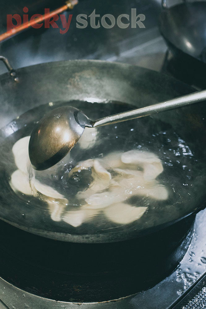 Chef uses ladle to cook dumplings in water of wok. 