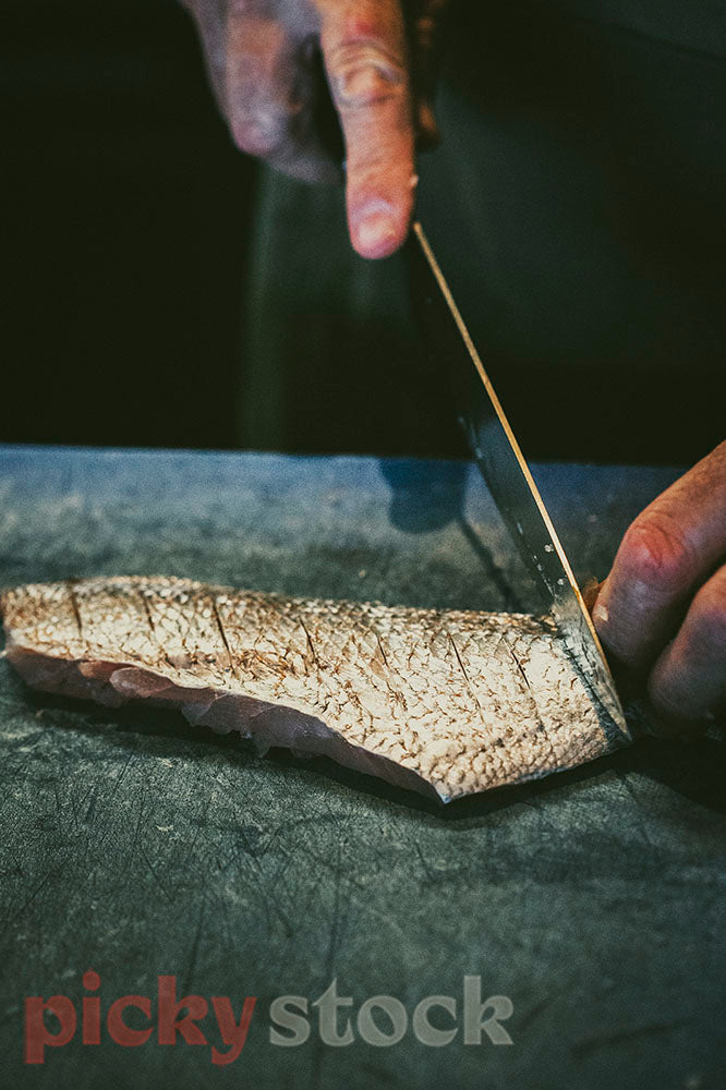Hand holds fish fillet, while other hand uses knife to cut into fillet. 