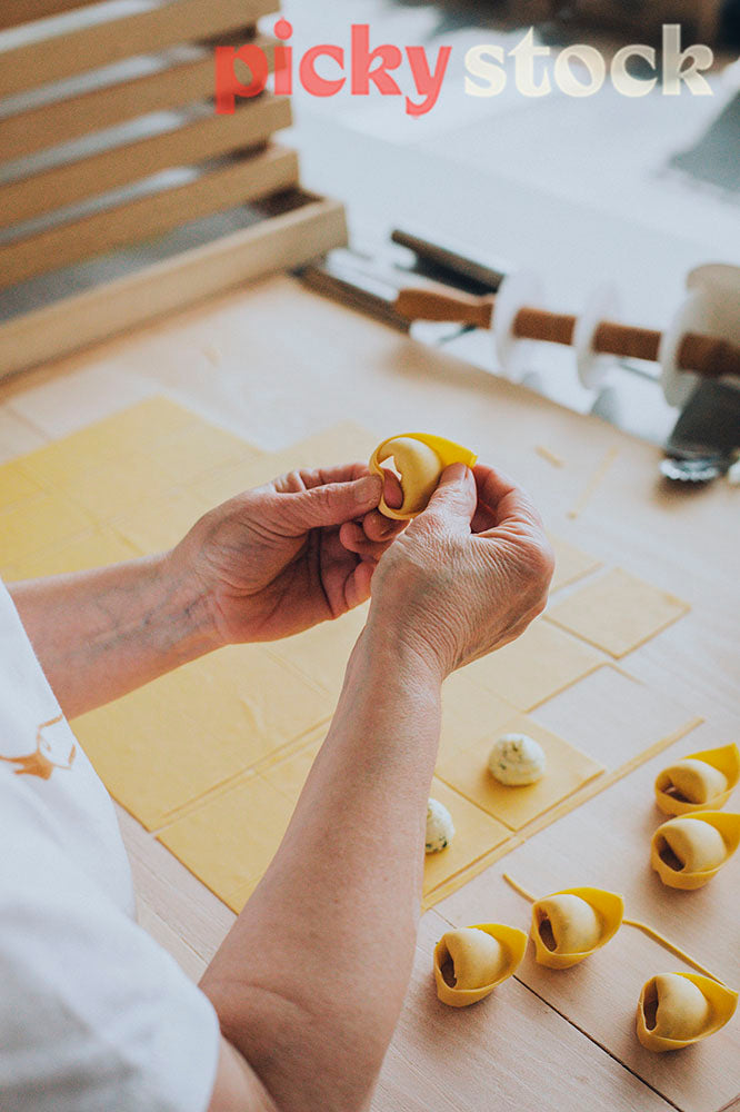 Looking over the shoulder of a chef, folding tortellini with their hands. 