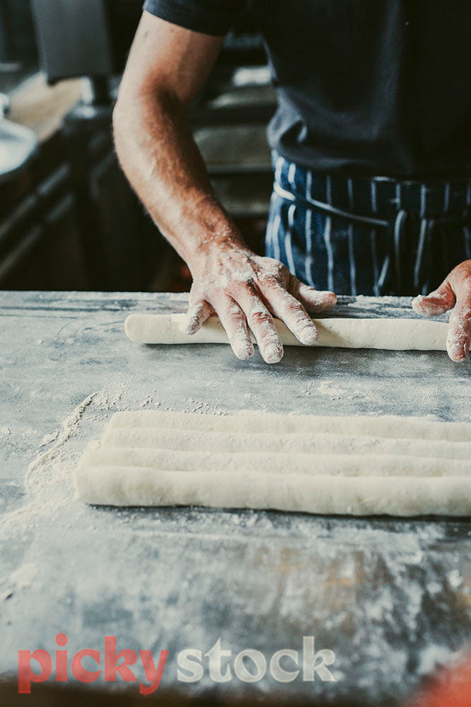Flour covered hands of chef rolling gnocchi dough into long thin rolls.