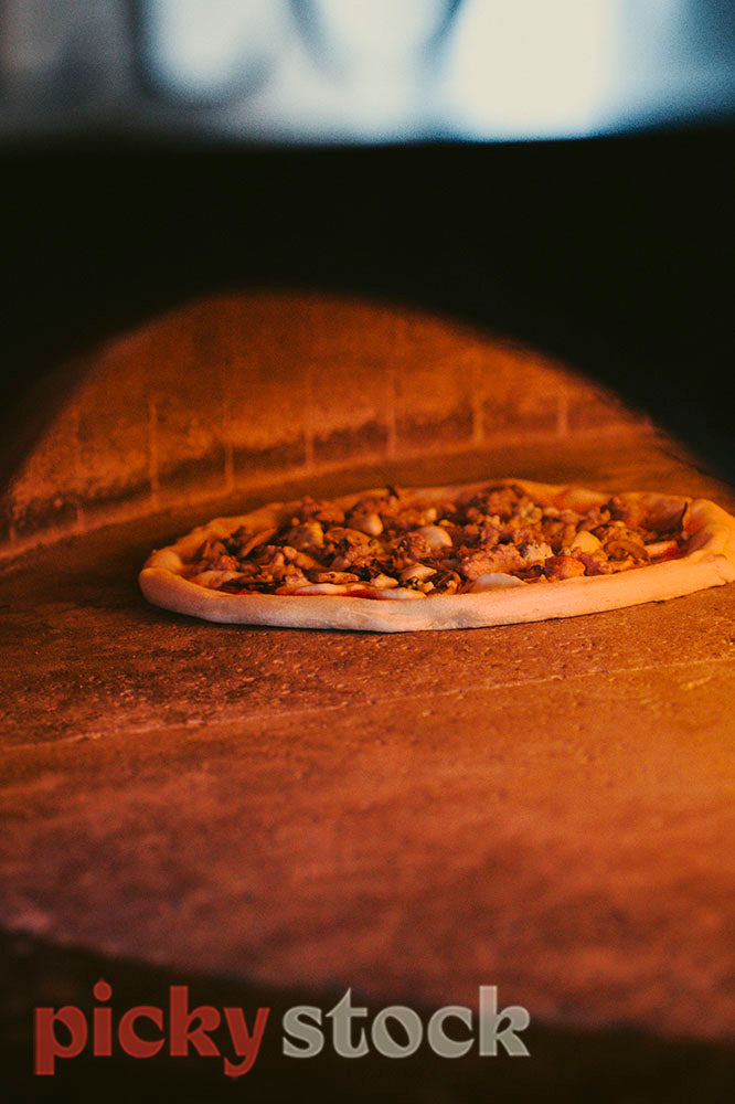 Pizza cooking in the golden / orange light of the woodfired oven.