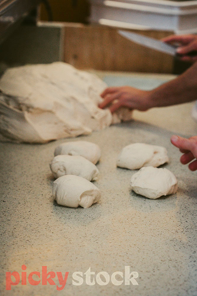 Chefs rolling pizza dough portions on bench with hands.