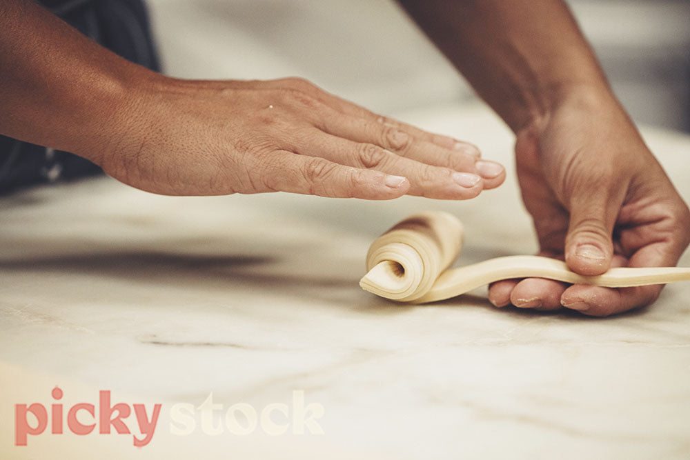 Pastry chef uses hands to roll croissant into shape.