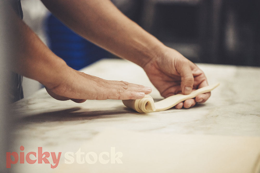 Hands rolling strips of pastry into croissants. 