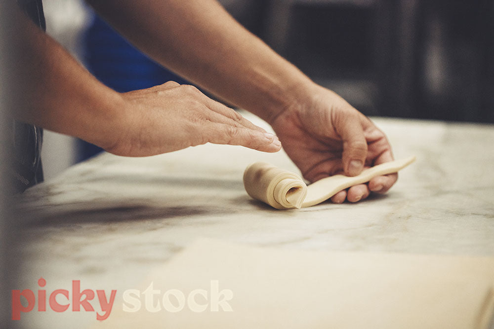Hands roll pastry into croissant. 