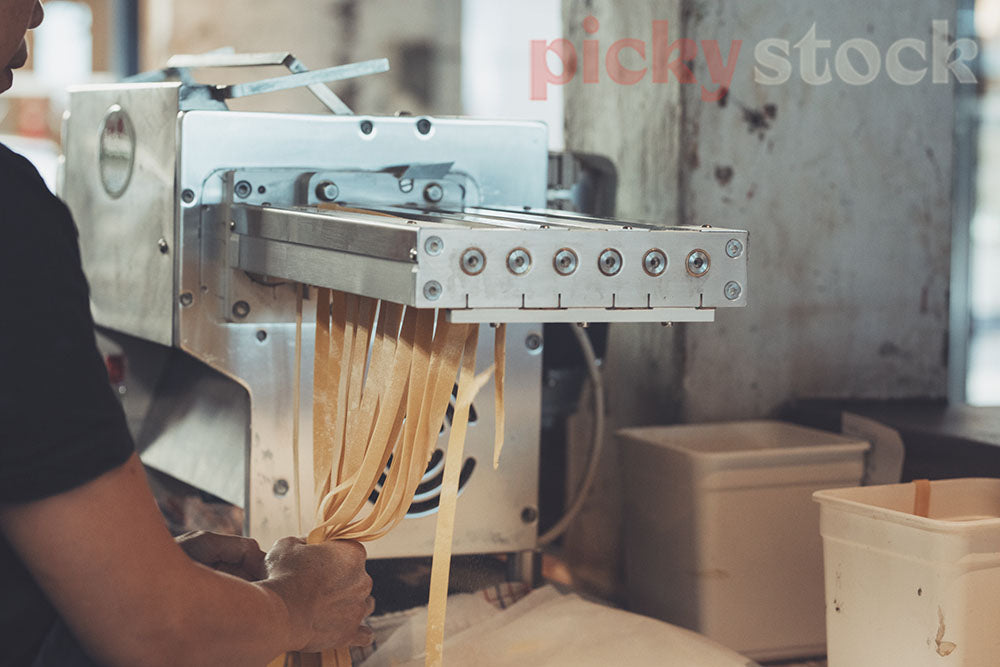 Chef uses pasta machine to make strips of Pasta. Using hands to pull out the strips. 